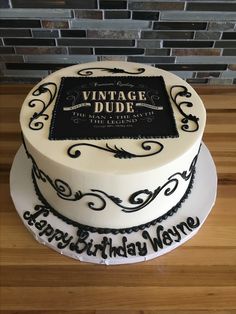 a white cake with black lettering on it sitting on top of a wooden table next to a brick wall