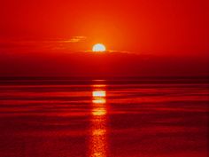 the sun is setting over the ocean on a red and black day with no clouds