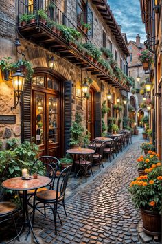 an alley way with tables and chairs lined up along the side of it, surrounded by potted plants