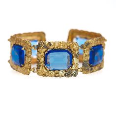 "Victorian in style, this beautiful vintage bracelet has vibrant dark blue glass set in yellow gold-plated silver. The chunky statement bracelet is decorated with flowers and would be a great piece for Spring or Summer. It's a great bracelet from the 1930s to add to your collection. The bracelet is in good vintage condition with some noticeable signs of wear. The gold plate has worn off on most elevated surfaces, exposing the silver underneath. These are small areas but are eye-visible. The spring ring clasp is fully functional but a little stiff. The glass has a few fine lines and marks, but nothing noticeable or obvious. There are no stamps or marks on the bracelet.  The bracelet measures 6\" long and 1\" wide and weighs 35.05 grams.  I try to portray the item accurately in its descripti Vintage Blue Jubilee Bracelet, Vintage Blue Bracelet For Formal Occasions, Vintage Blue Bangle Bracelets, Vintage Blue Jewelry With Jubilee Bracelet, Vintage Blue Bracelets For Party, Vintage Blue Jubilee Bracelet Jewelry, Antique Blue Bracelet Jewelry, Formal Blue Jeweled Bracelets, Formal Blue Costume Jewelry Bracelets