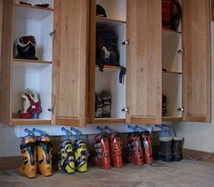 several pairs of ski boots are lined up on the floor in front of wooden cabinets