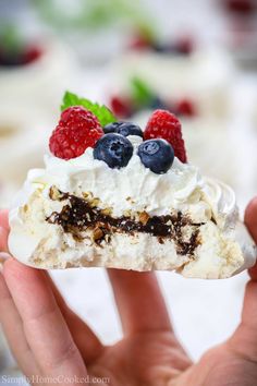 a person holding up a piece of cake with berries on top and whipped cream in the middle