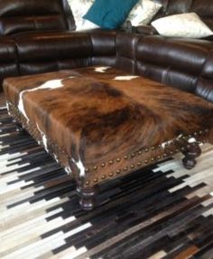 a cow hide ottoman sitting on top of a rug in front of a leather couch