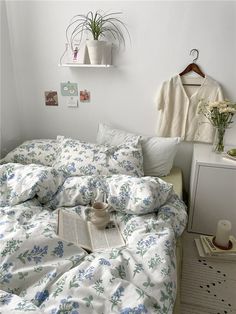 an unmade bed with blue and white flowers on the comforter next to a book