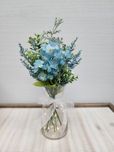 a clear vase with blue flowers and greenery