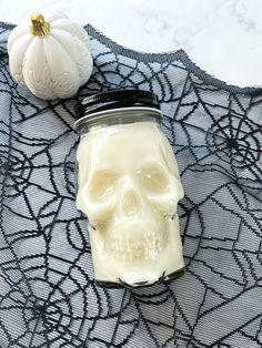 a glass jar filled with liquid next to a white pumpkin on a lace tablecloth