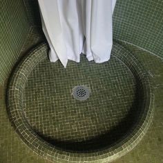 a green tiled bathroom with a drain in the floor