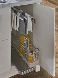 an open cabinet in a kitchen with towels hanging on the rack and cleaning supplies inside