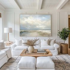 a living room filled with white furniture and a painting hanging on the wall above it