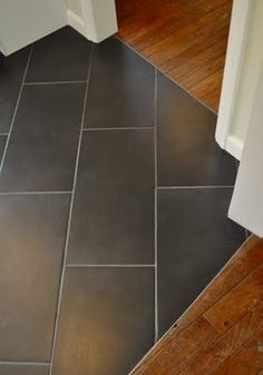 a black tile floor in a bathroom next to a white door and toilet paper roll