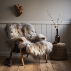 a chair with some fur on it in front of a wall and a vase filled with flowers