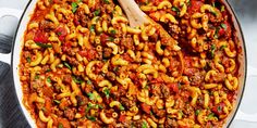 a large pot filled with pasta and meat in tomato sauce next to a wooden spoon