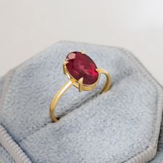 a gold ring with a red stone in it on top of a blue velvet bag