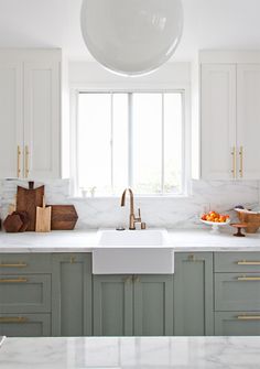 a kitchen with marble counter tops and green cabinets, gold pulls on the faucet