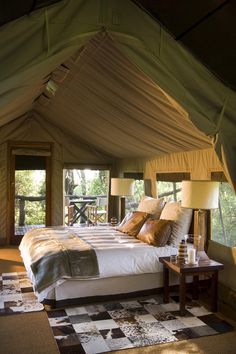 a large bed sitting inside of a tent next to a table with two lamps on it