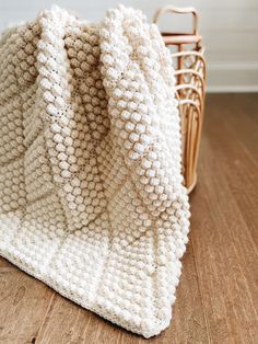 a white knitted blanket sitting on top of a wooden floor next to a basket