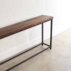 a wooden bench sitting on top of a cement floor next to a white walled wall