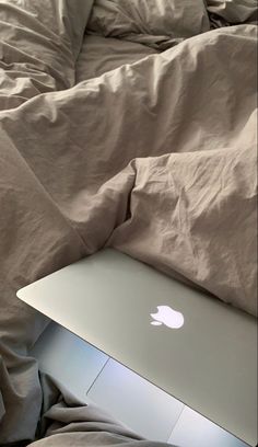 an apple laptop sitting on top of a bed covered in blankets and sheets with the cover pulled down