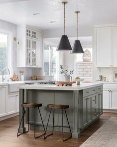 a kitchen with two stools in front of an island and white cabinets, along with black pendant lights hanging from the ceiling