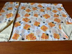 an orange and white flowered table runner on a wooden floor with two pieces of cloth folded over it