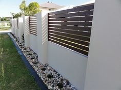 a white fence with rocks and grass in front of it on the side of a house