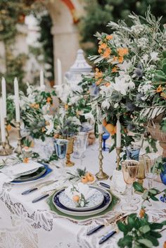 the table is set with white and blue plates, silverware, orange flowers and greenery