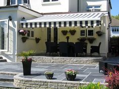 an outdoor patio with black and white striped awning over the dining area, surrounded by potted plants