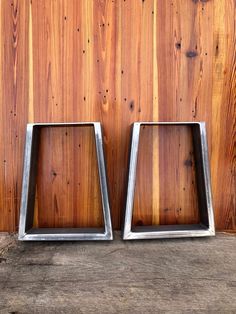 two square metal frames sitting on top of a wooden table next to a wall covered in wood planks