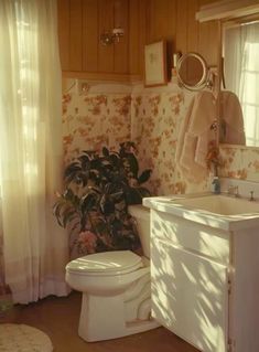 a white toilet sitting next to a sink in a bathroom under a window with curtains