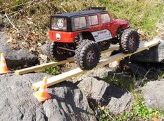 a red toy truck driving on top of a wooden bridge over rocks with cones around it