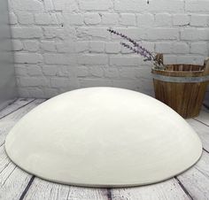 a white round object sitting on top of a wooden table next to a basket with flowers