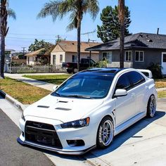 the white car is parked on the side of the street in front of some palm trees