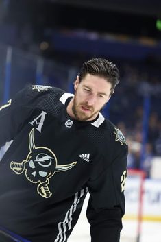 a man in black jersey standing on ice with his hands behind his back and looking at the camera