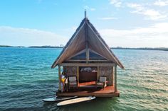 a man standing on top of a boat next to a small hut in the water