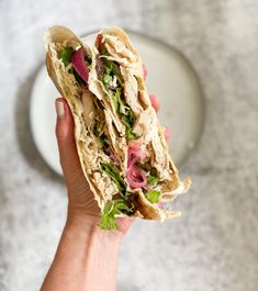 a hand holding a sandwich with meat and veggies in it on a plate