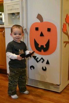 a little boy standing in front of a refrigerator with a cat on it's arm