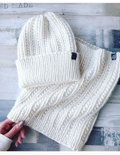 a white knitted hat and scarf laying on top of a wooden floor next to a person's hand