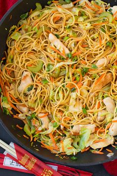 a wok filled with noodles and vegetables next to chopsticks