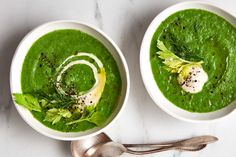 two white bowls filled with green soup on top of a table