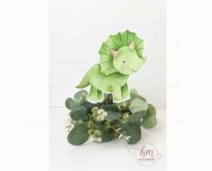 a small green toy dinosaur sitting on top of a plant with leaves and flowers in front of it