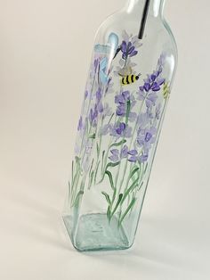 a glass bottle with purple flowers painted on the side and a bee flying over it