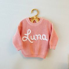 "Personalized Hand Embroidered Baby and Toddler Knit Sweater or Onesis.    Preorder for shipping in 2 weeks, please contact us if you need it for a specific date to check accommodations Our adorable hand-embroidered name sweaters are perfect for newborn photography, first birthdays, family photos, baby shower gifts, birthday gifts, or any occasion! This is a 100% Cotton Knit, always made with love and care for your baby's skin. Embroidery is done by hand and can vary.  Every sweater is one of a kind as they are all customized with name. One name or word is made with Chunky Yarn for a relieved look, and the letter \"i\" can be made with a daisy on top by request.  Add daisies all over option is available too.  Longer names or 2 names are made with a regular yarn. Max 2 names. We love to fit Pink Long Sleeve Sweater With Embroidered Logo, Cute Long Sleeve Embroidered Sweater, Pink Winter Sweater With Embroidered Logo, Cute Winter Sweater With Embroidered Text, Hand Knitted Long Sleeve Pink Tops, Pink Hand Knitted Long Sleeve Tops, Long Sleeve Pink Sweater With Embroidered Text, Pink Long Sleeve Sweater With Embroidered Text, Pink Embroidered Long Sleeve Sweater