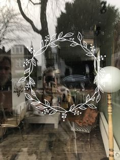 the reflection of a person sitting at a table in a store window with a wreath on it