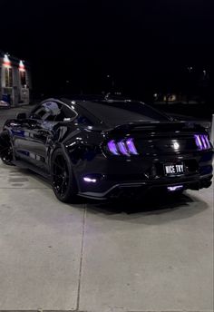 a black mustang parked in front of a gas station at night with its lights on