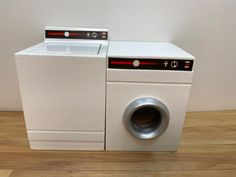 two washing machines sitting next to each other on top of a wooden floor in front of a white wall