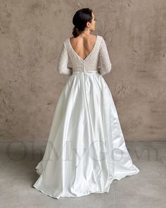 a woman in a white wedding dress standing against a wall with her back to the camera