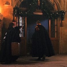 two men in robes are standing outside an old building with christmas wreaths on the door