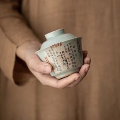 a person holding a tea cup with writing on the side and in their hands, against a brown background