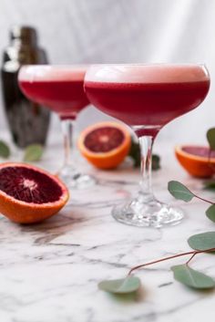 three wine glasses filled with blood oranges and garnished with greenery on a marble table