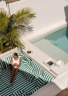 a woman sitting on top of a green and white striped blanket next to a pool